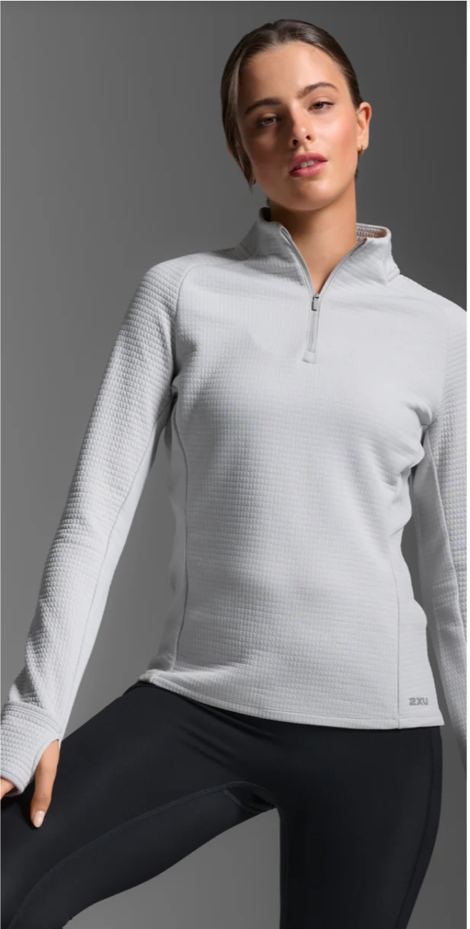 Woman wearing a light gray long-sleeve athletic top with a quarter zip on a gray background