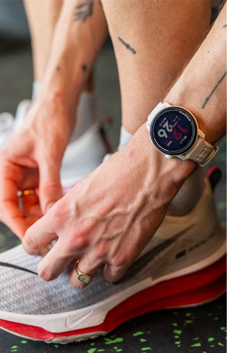 Person tying running shoes with a Coros Pace 3 watch, outdoors.