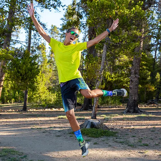 Courtney Dawaulter in bright yellow shirt and colorful socks jumping in a forest