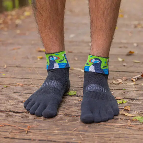 Person wearing black toe-separated socks with colorful designs on a wooden floor.