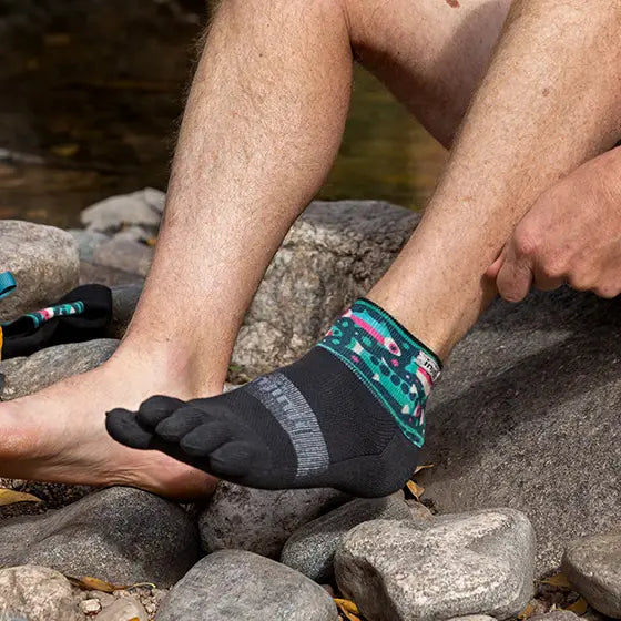 Person wearing black and teal socks sitting on rocks near water