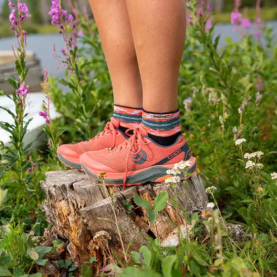 Person wearing pink hiking shoes on a log with a natural background of flowers and greenery