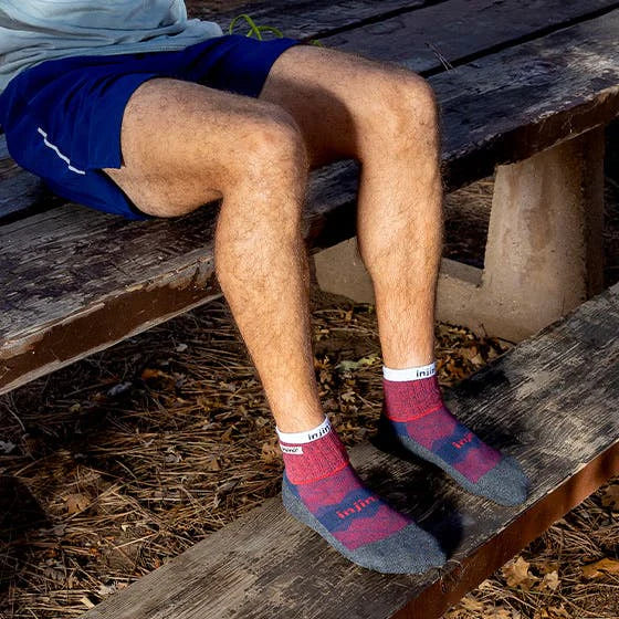 Person wearing red and gray checkered socks sitting on a wooden bench outdoors.