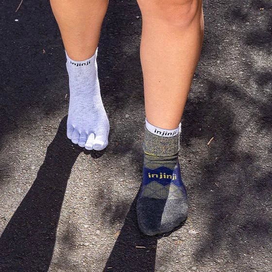 Person wearing gray and blue injinji socks on a dark surface