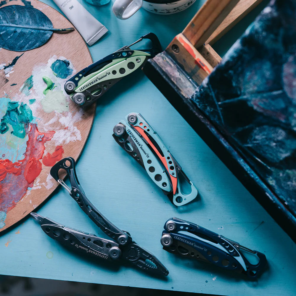 Collection of multi-tool knives on a blue surface with art supplies in the background
