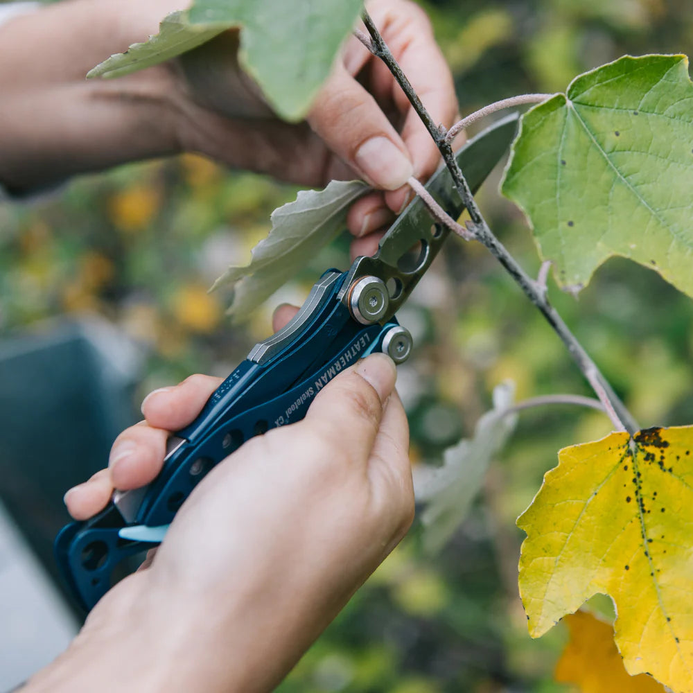 Person using a blue multi-tool to trim a branch with green and yellow leaves.