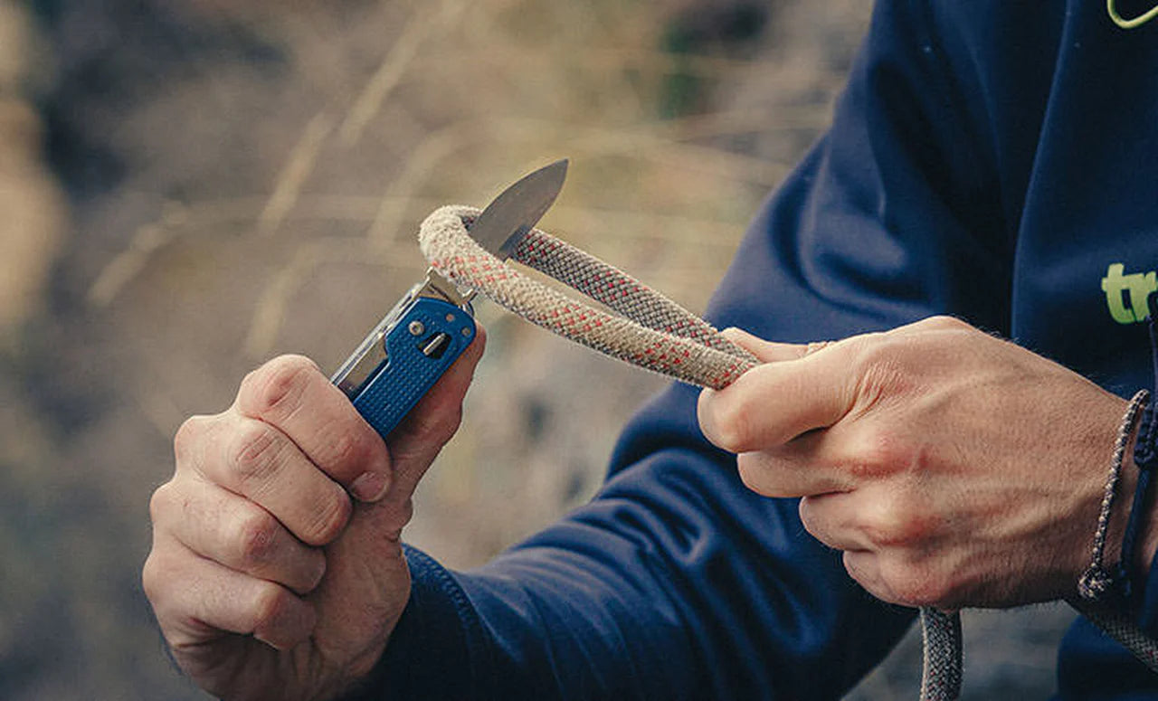 Person using a knife to cut a rope with a blurred natural background