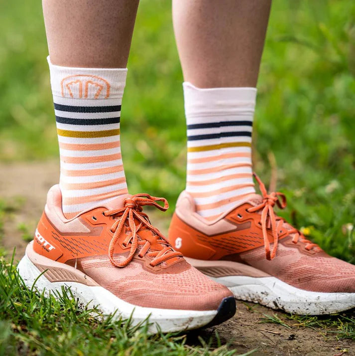 Orange running shoes with striped socks on a grassy background