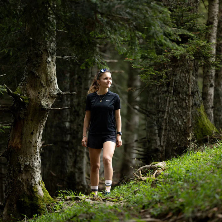 Woman walking through a forest path with trees and greenery around her.