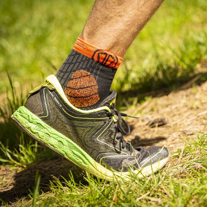 Person wearing a black and green athletic shoe with orange accents on a grassy path.