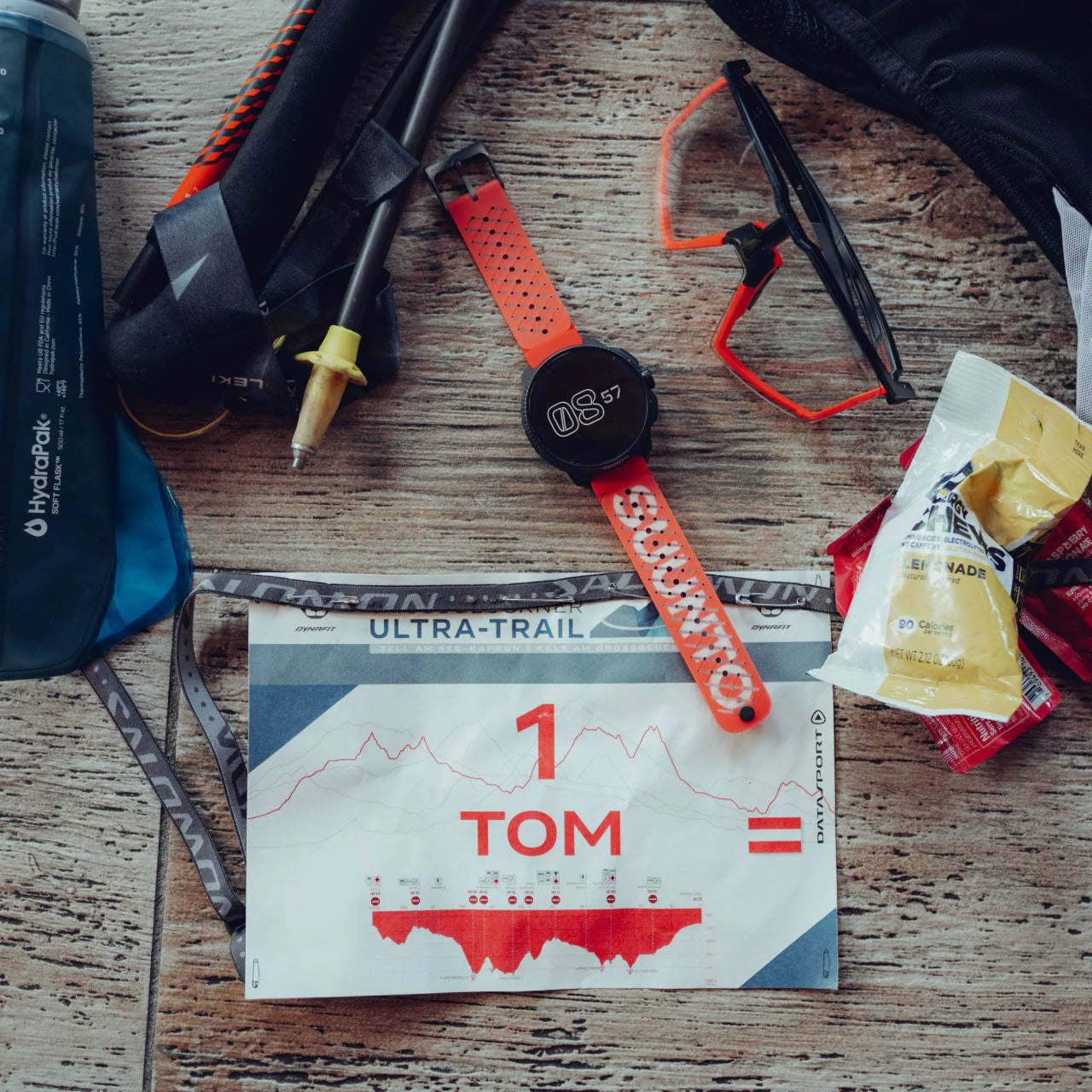 Trail running gear including a watch, map, and snacks on a wooden surface