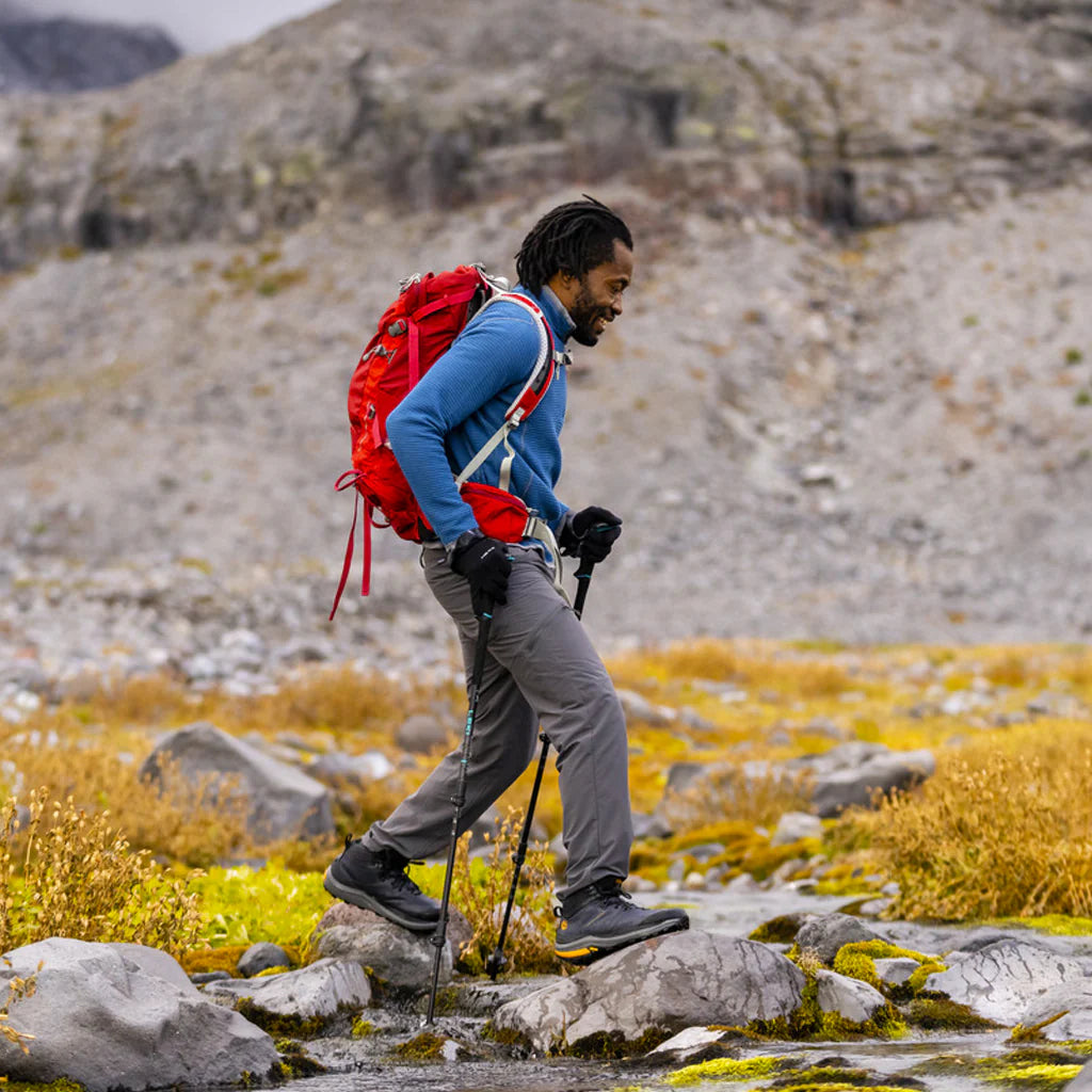 Man hiking on a rocky trail with a red backpack in a mountainous landscape