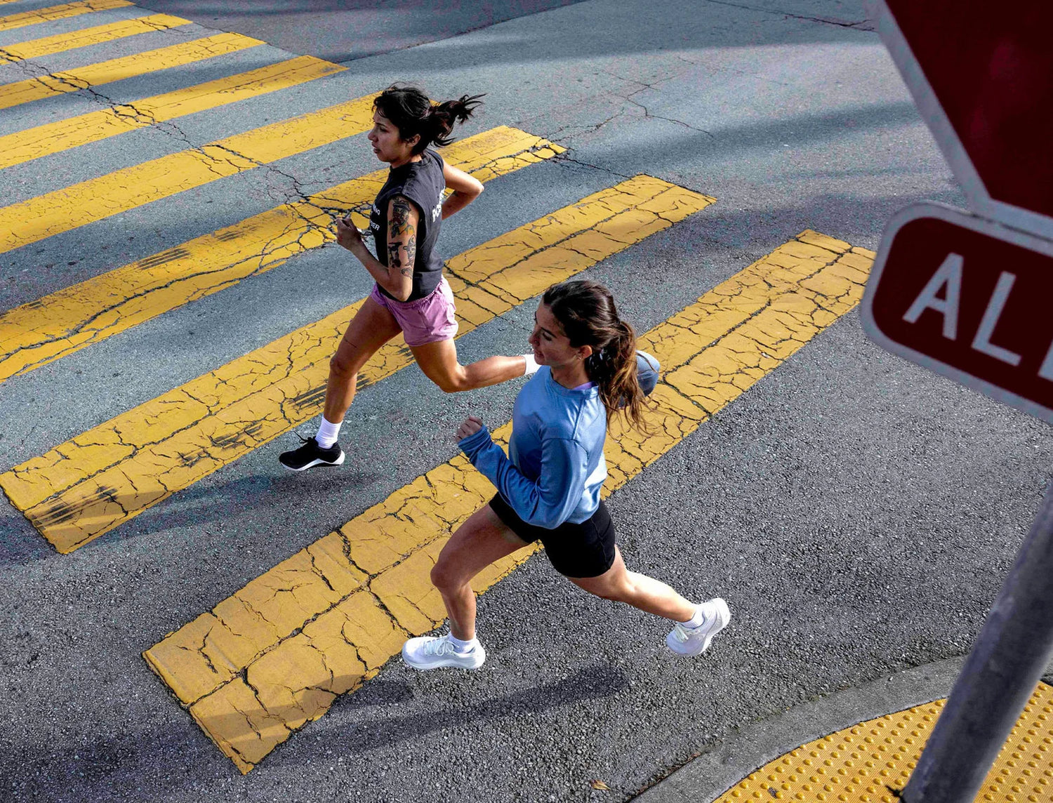 Two women running on a crosswalk with a stop sign in the foreground.