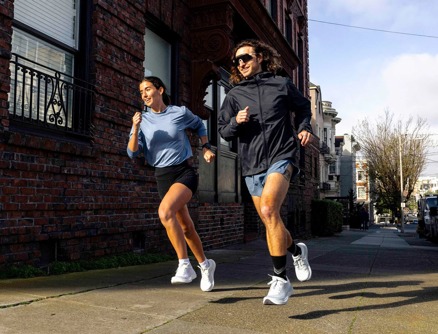 Two people running on a sidewalk in an urban setting.